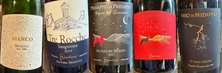 A selection of five wine bottles with distinctive labels, including Bianco, Tre Rocche Sangiovese 2019, Predappio di Predappio Superiore Riserva 2017, Predappio Riserva, and Nero di Predappio In Vino Veritas. The labels feature various designs and colors, showcasing the winery Fattoria Nicolucci.