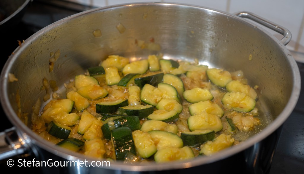A pot filled with diced zucchini and yellow squash sautéing with onions on the stovetop.