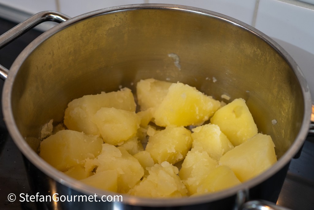 Potatoes in a large pot, partially cooked, ready for mashing.