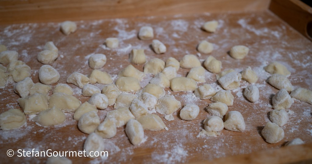 Freshly made gnocchi scattered on a wooden surface dusted with flour.