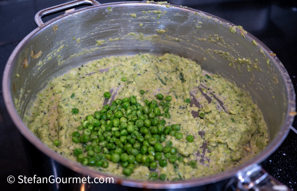 A large pot on a stovetop containing a green, creamy mixture with fresh green peas added on top.