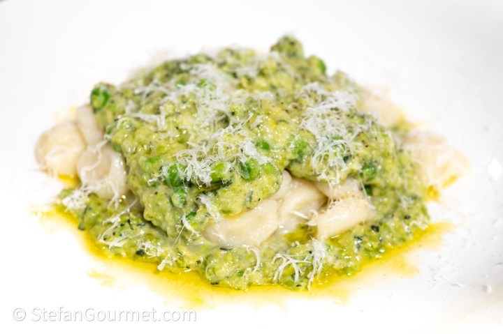 A serving of gnocchi topped with a vibrant green pesto sauce and grated cheese, presented on a white plate.