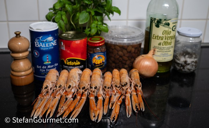 A collection of cooking ingredients including fresh shrimp, herbs, spices, salt, olive oil, and an onion, arranged on a kitchen countertop.