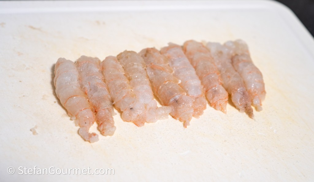 Fresh shrimp laid out on a cutting board, showcasing their translucent and pinkish color.
