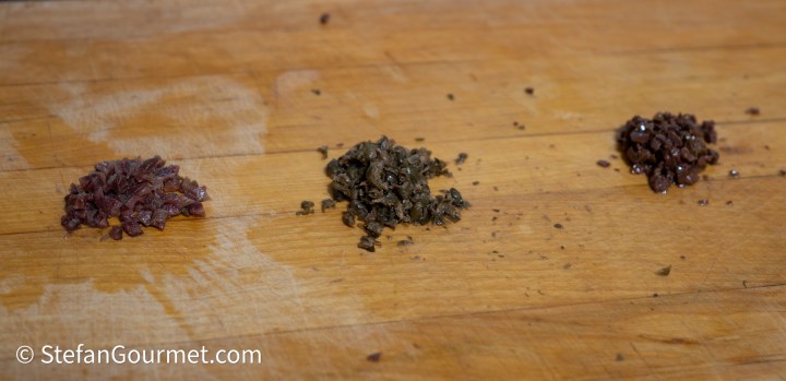 Three piles of finely chopped ingredients on a wooden surface, showcasing different colors and textures.