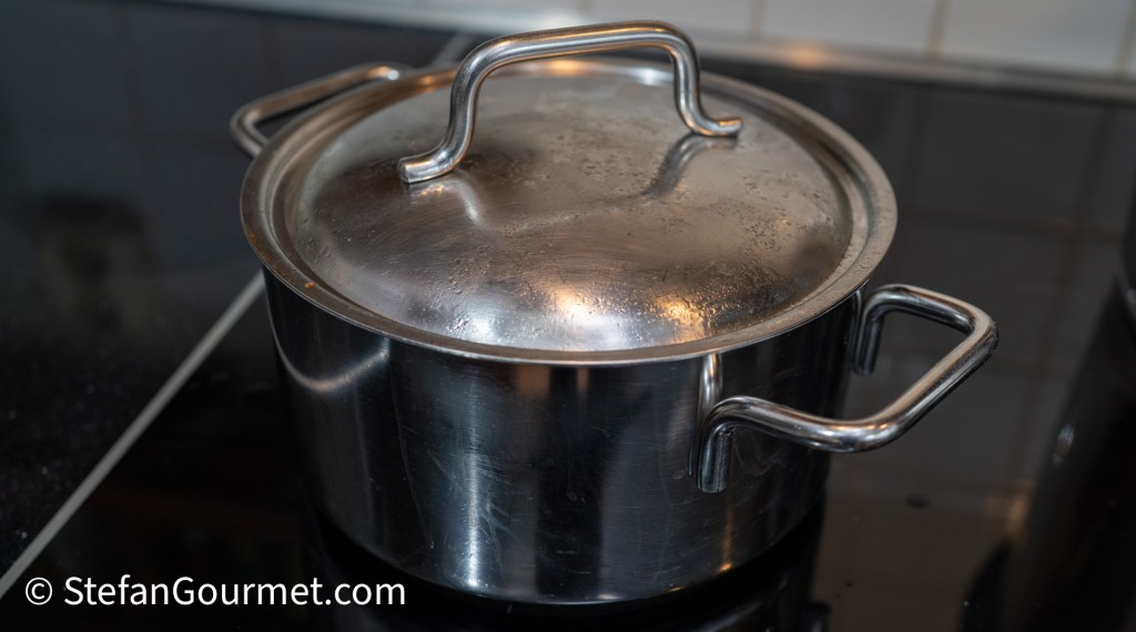 A stainless steel pot with a lid, sitting on a stovetop surface.
