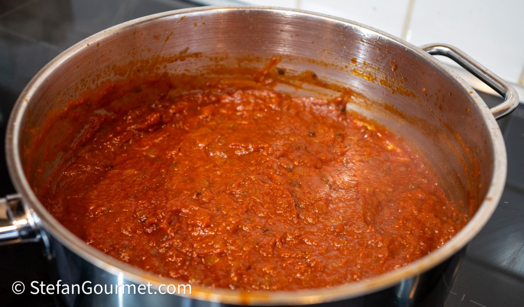 A large pot filled with simmering red sauce on a stovetop.
