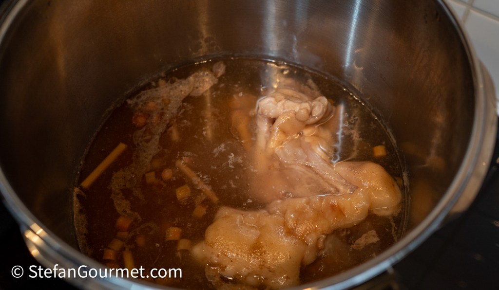 A close-up view of a pot containing chicken parts simmering in a broth with vegetables.