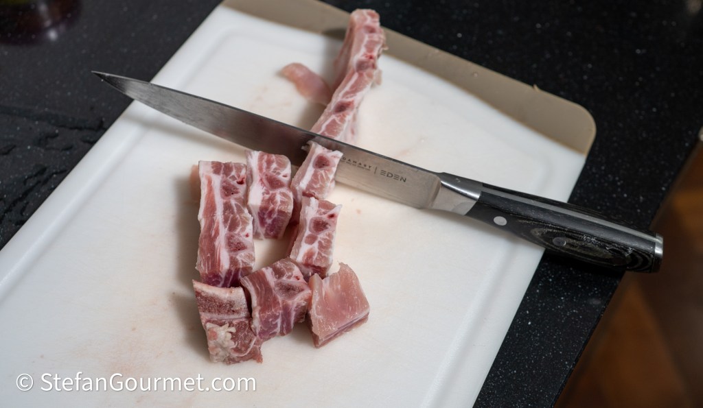 Chopped pieces of pork belly arranged on a cutting board next to a chef's knife.