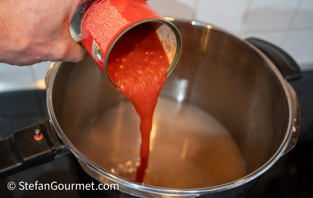 A person pouring canned tomato sauce into a pot on a stovetop.