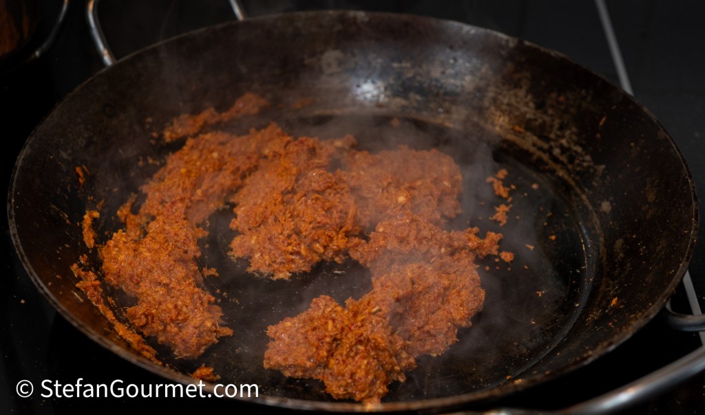 A pan with sizzling and steaming cooked ground meat mixture, displaying a rich reddish-brown color.