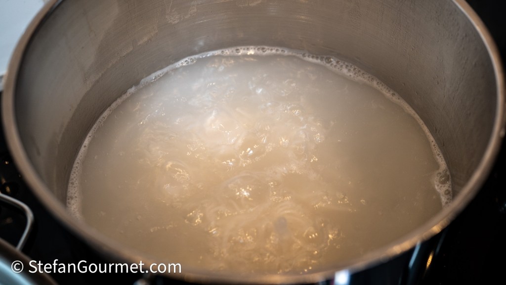 A close-up view of a pot filled with boiling water, creating bubbles and steam.
