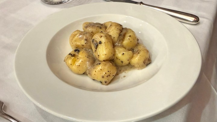 A plate of gnocchi served in a creamy sauce with black pepper, placed on a white plate.
