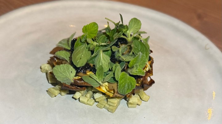 A beautifully plated dish featuring layers of artichoke topped with vibrant green herbs and garnishes, served on a white plate.