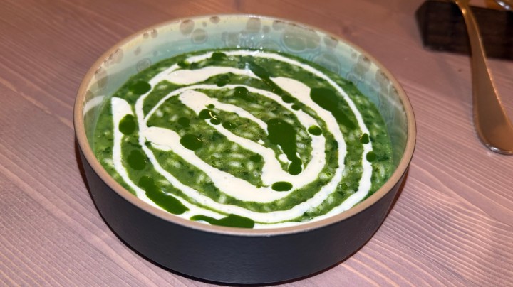 A bowl of green soup garnished with swirls of cream and drizzles of green oil.