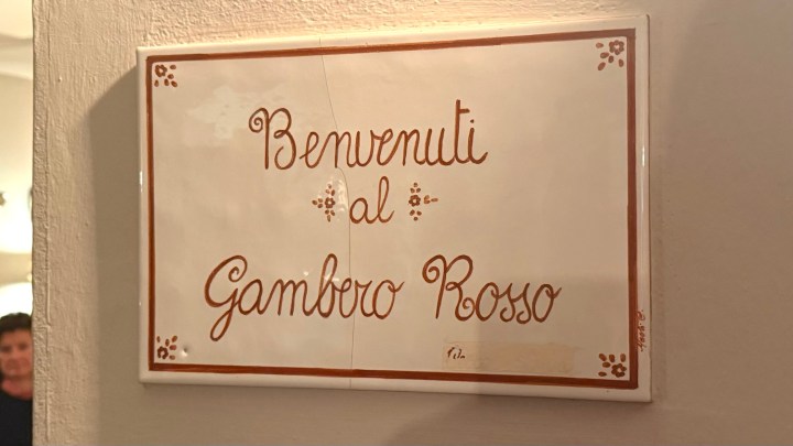 A ceramic sign that says 'Benvenuti al Gambero Rosso' which translates to 'Welcome to the Red Shrimp'.