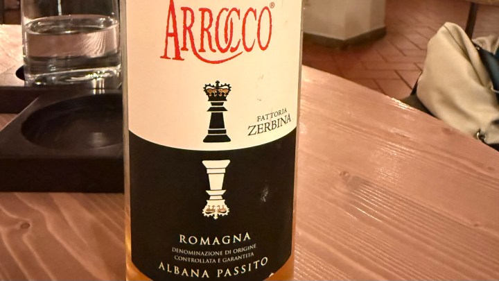 A close-up of a bottle of Arrocco Albana Passito wine, showcasing the label details and brand name, placed on a wooden table.