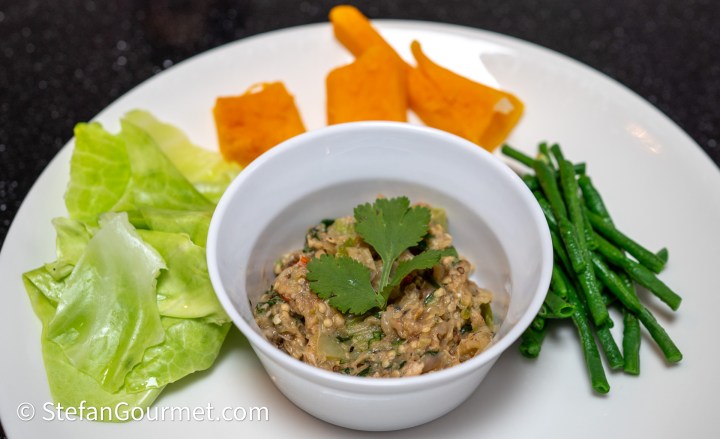 A white plate featuring a bowl of green vegetable dip garnished with cilantro, accompanied by steamed green beans, lettuce leaves, and slices of roasted orange squash.