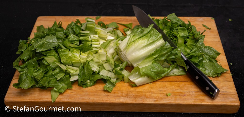 Chopped romaine lettuce on a wooden cutting board with a chef's knife.