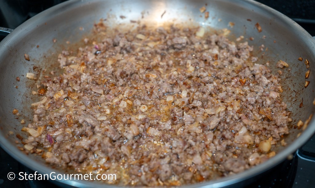 Cooked ground meat mixed with finely chopped onions in a frying pan.