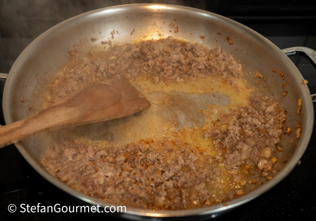 A skillet with browned ground meat and a wooden spoon, steaming on a stovetop.
