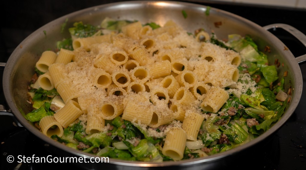 A skillet filled with pasta rigatoni mixed with sautéed greens and topped with grated cheese.