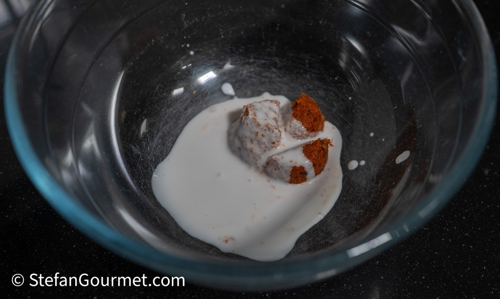 A glass bowl containing a piece of brown dough partially submerged in white liquid.