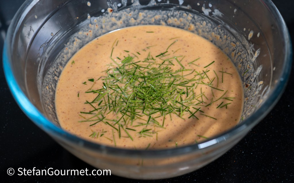 A clear glass bowl containing a mixture with a creamy texture, topped with finely chopped green herbs.