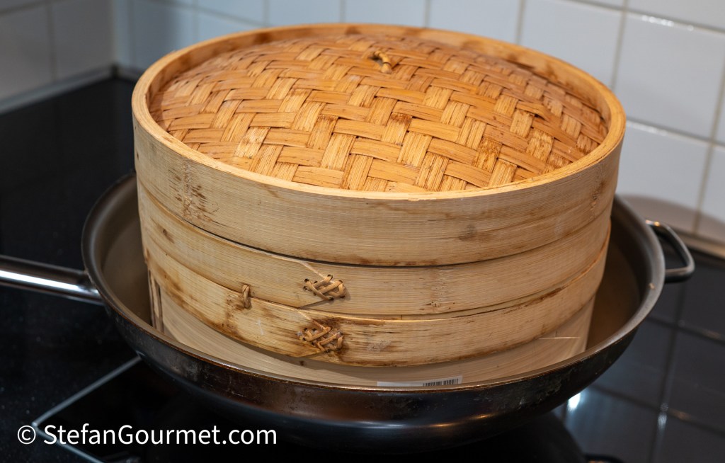 A bamboo steamer stacked on top of a pot on a stovetop, ready for cooking.