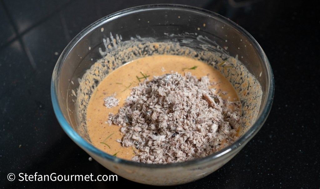 A glass bowl containing a mixture of creamy sauce and shredded meat, set on a dark countertop.