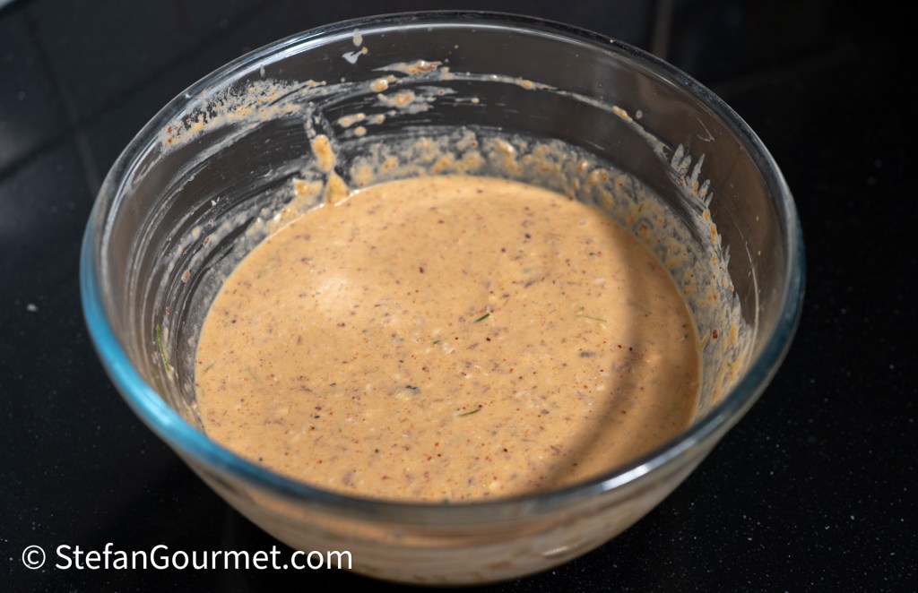 A glass bowl containing a thick, creamy mixture with a light brown color, placed on a dark countertop.