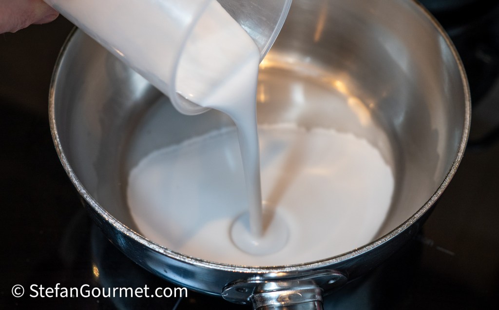 A person pouring liquid into a stainless steel pot on a stovetop.