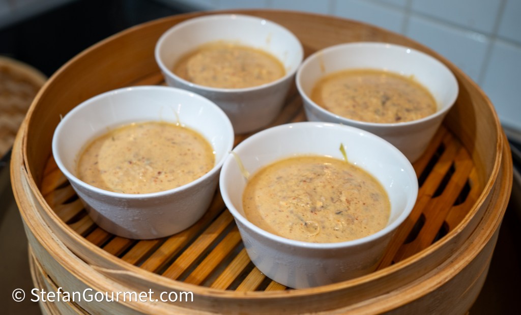 Four white bowls filled with a creamy, textured mixture, placed inside a bamboo steamer.
