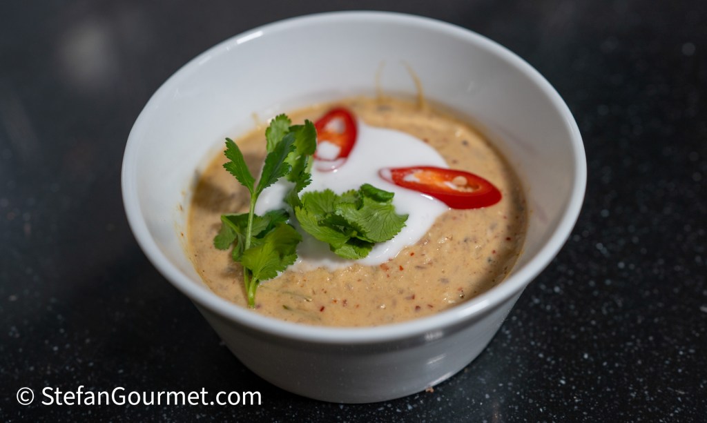 A bowl of creamy soup topped with fresh cilantro, sliced red chili, and a swirl of yogurt.