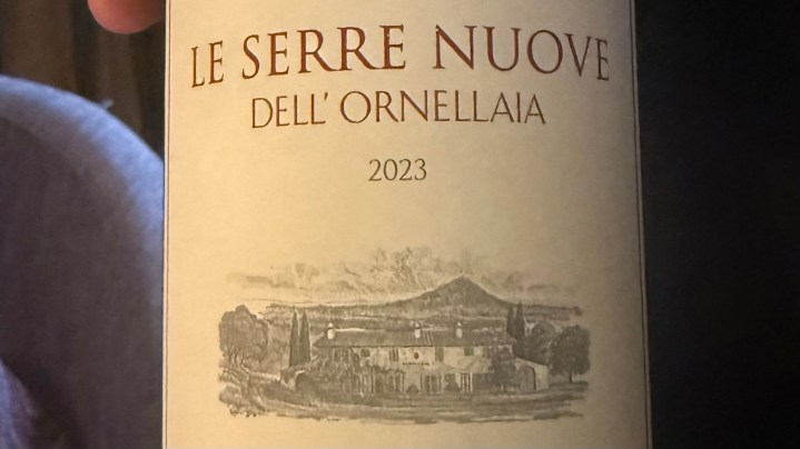A close-up of a wine bottle label featuring 'Le Serre Nuove dell'Ornellaia 2023' with a detailed illustration of a winery.