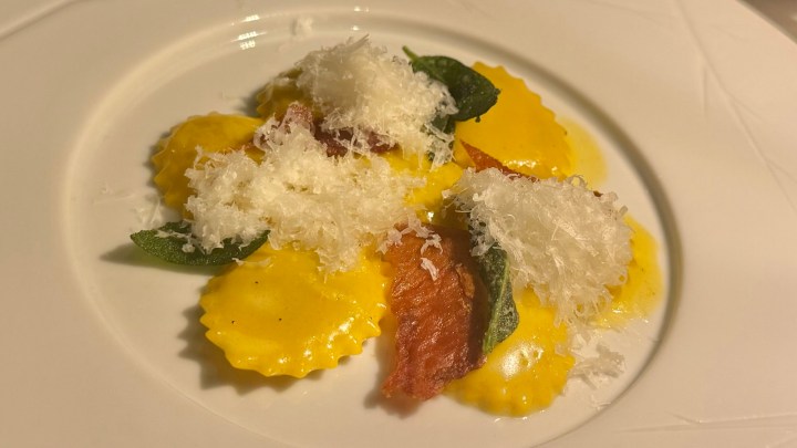 Plate of ravioli topped with grated cheese and crispy sage leaves.
