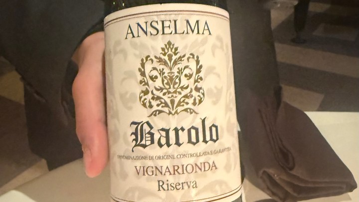 A hand holding a bottle of Anselma Barolo Vignarionda Riserva wine, featuring an ornate label with decorative elements.
