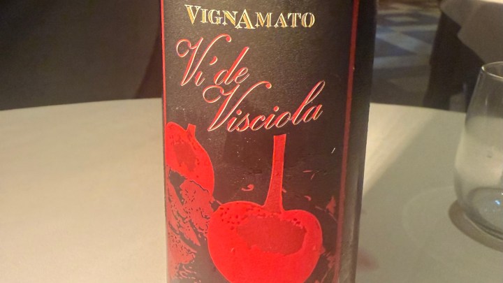 Close-up of a wine bottle labeled 'Vignanato Vi de Visciole', featuring a black background with red cherry illustrations