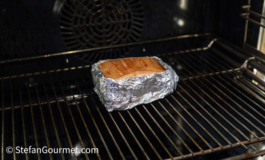 Salmon fillet wrapped in aluminum foil, placed on the rack inside an oven.