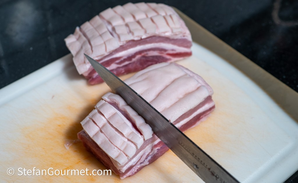A chef slicing a piece of pork belly on a cutting board, showcasing the layers of fat and meat.