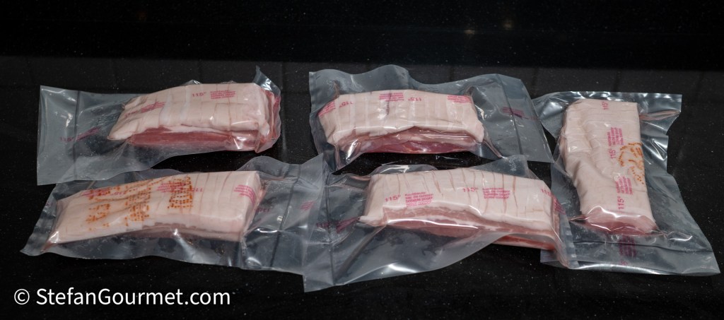 Vacuum-sealed packages of pork belly, arranged on a black countertop.