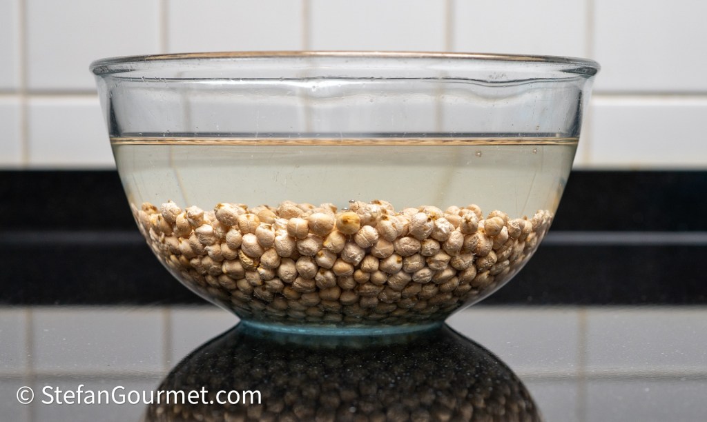 A glass bowl filled with water and dried seeds soaking inside, placed on a dark countertop.