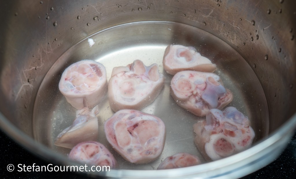 A stainless steel pot filled with water and several pieces of raw bone marrow, partially submerged.
