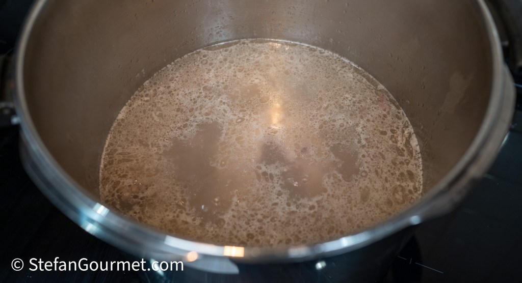 A close-up view of a pot filled with simmering broth, showing bubbles and steam on the surface.