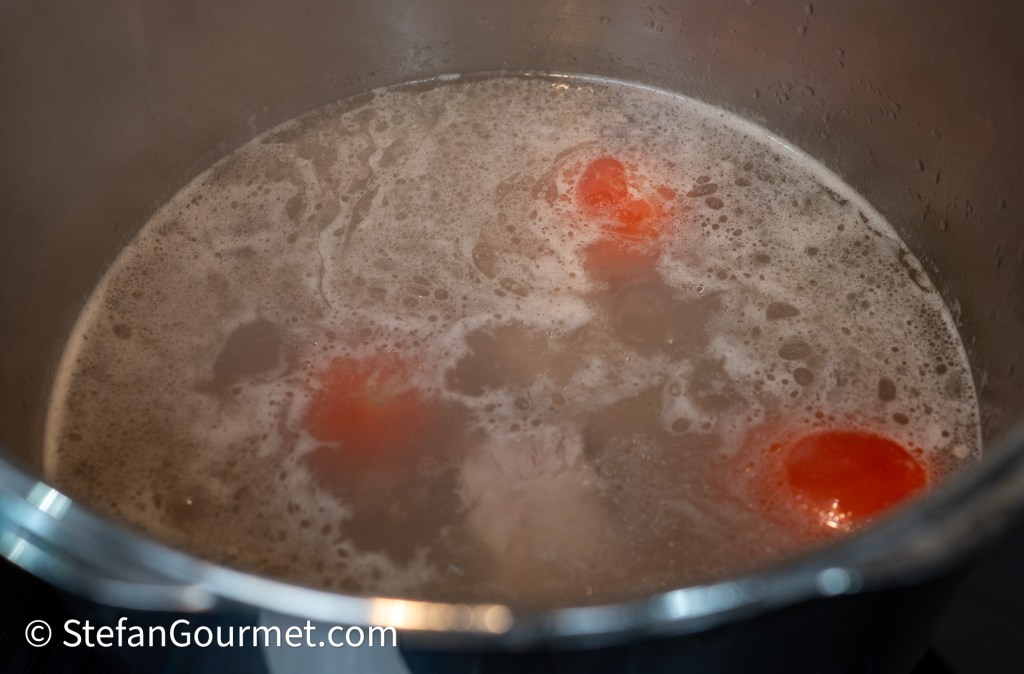 A pot of boiling broth with floating whole red tomatoes and bubbles on the surface.