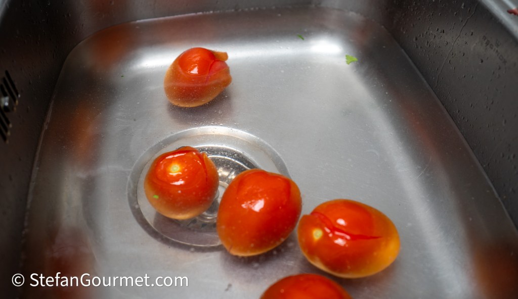 A stainless steel sink filled with water, containing several small, round, orange tomatoes.