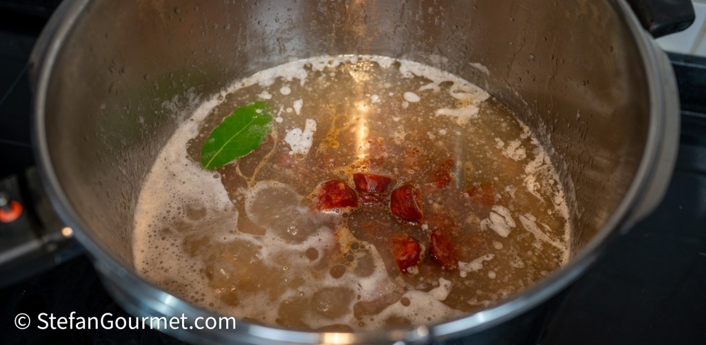 A pot on the stove containing simmering broth with bay leaves and dried ingredients, producing steam and bubbles.