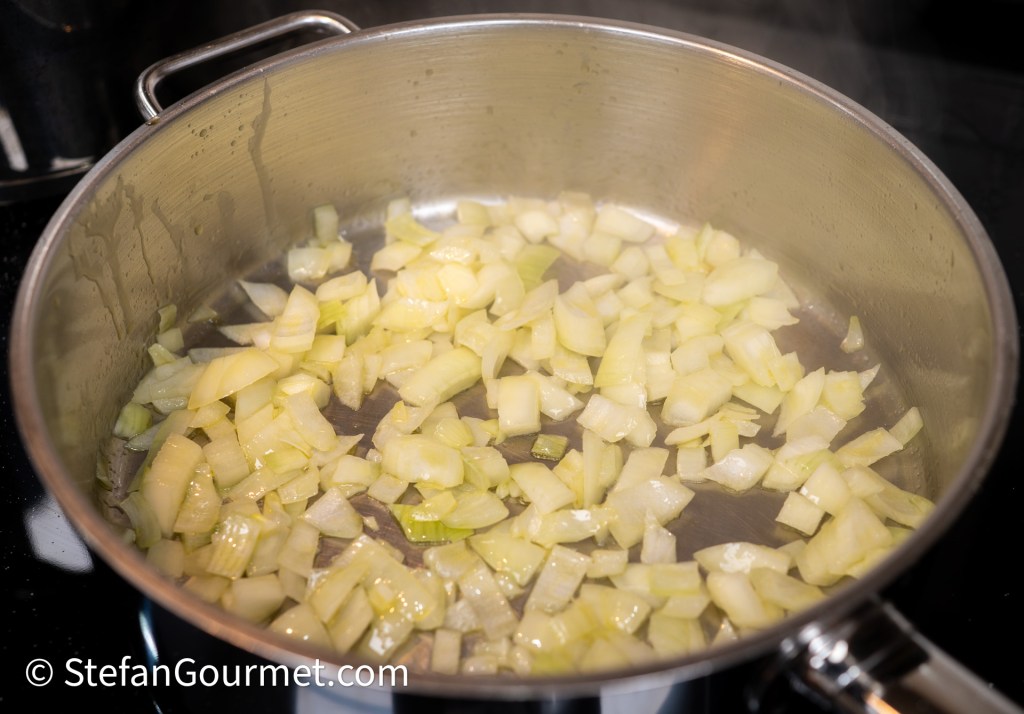 Chopped onions cooking in a stainless steel pan on a stovetop.
