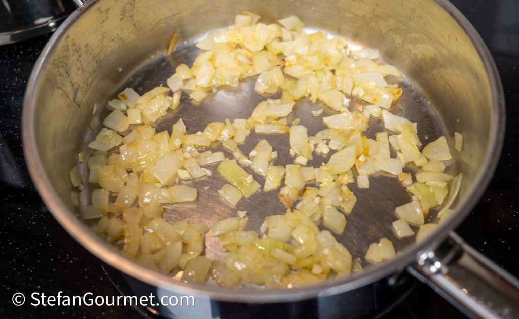 Sautéed chopped onions in a stainless steel pan on a stovetop.