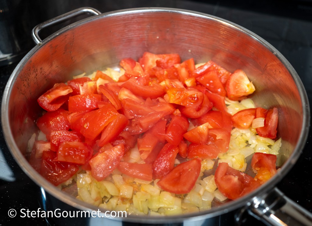 A close-up of a pot with chopped tomatoes and onions cooking on a stovetop.